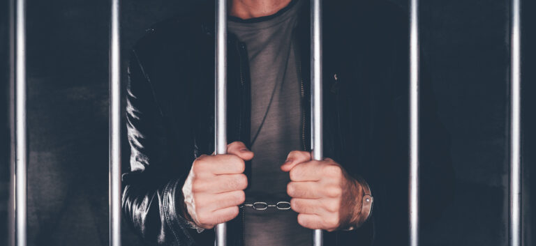 Handcuffed man behind prison bars